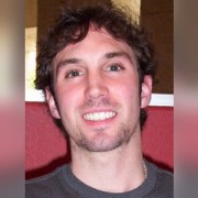 Smiling man with wavy dark hair and scruffy facial hair